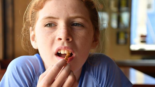 Teen girl putting food in her mouth with her eyebrows scrunched looking uncertain.