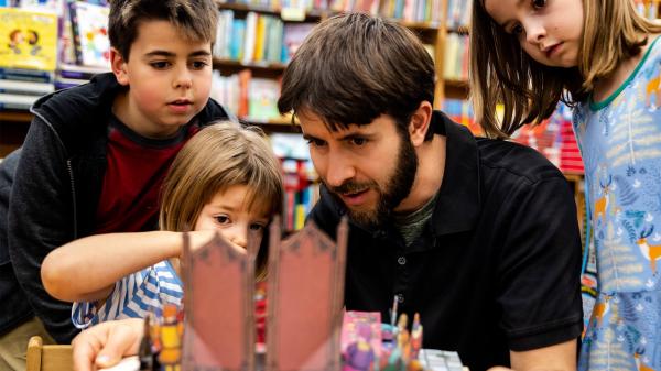 Man and three kids gaze at pop-up castle book