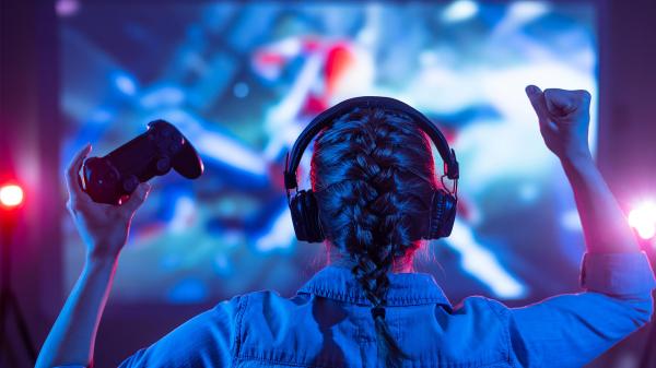 Back view of girl in headphones playing a video game on a TV screen.