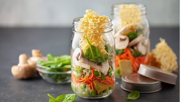 Two mason jars filled with fresh vegetables and ramen noodles.