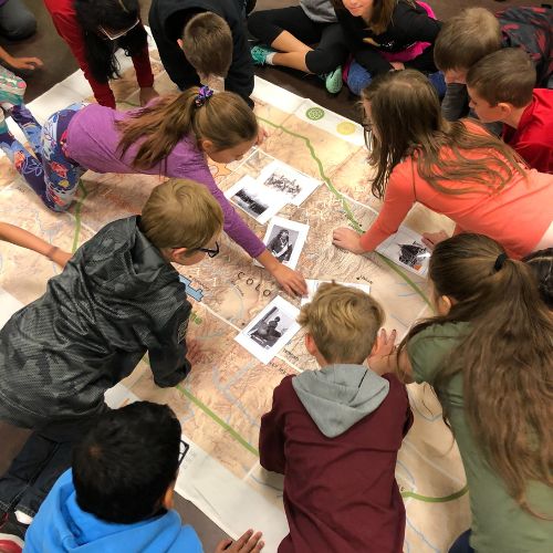 Children examining large Colorado map and Native American images.