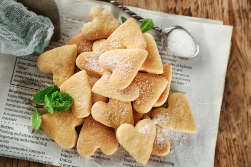 Heart shaped butter cookies on recipe sheet with decorative mint leaves and a spoon. 