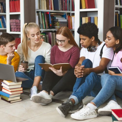 Teens sitting together on the floor at the library looking at a book
