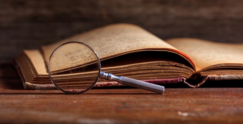 Vintage book and magnifying glass on wooden desk.