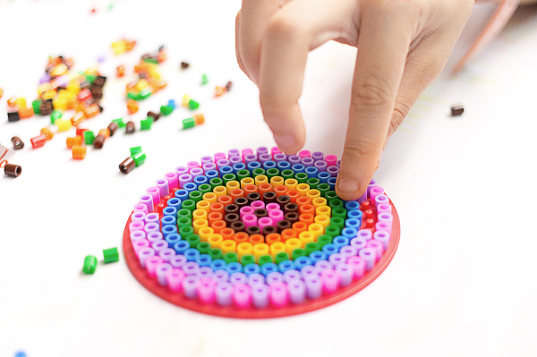 Colorful perler bead design on round pegboard with hand placing beads.