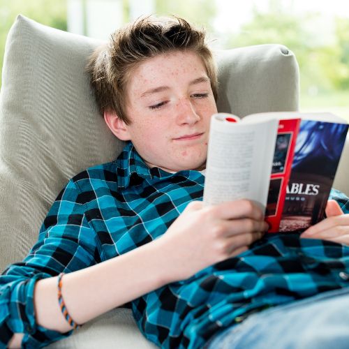 Teen boy reading a book while lounging on a couch.