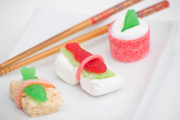 3 colorful candy sushi rolls with candy fish on top with wooden chopsticks in the background. 