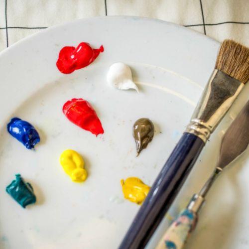 White plate with dabs of paint, paint brush and paint scraper