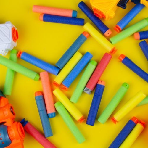 Nerf blasters and darts laying on a yellow table.