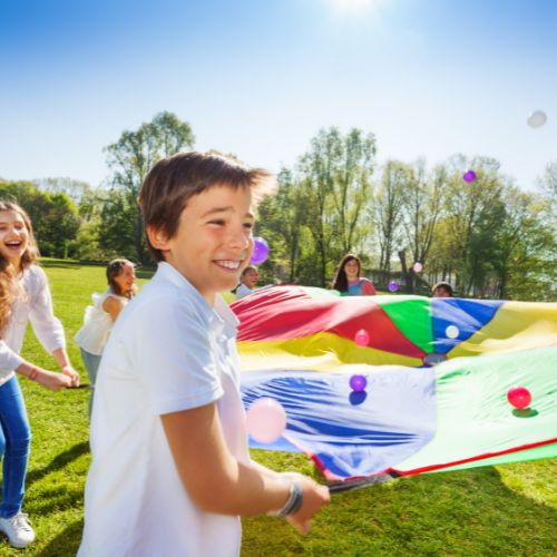 Children playing outside on the grass on a sunny day using a parachute and balls.