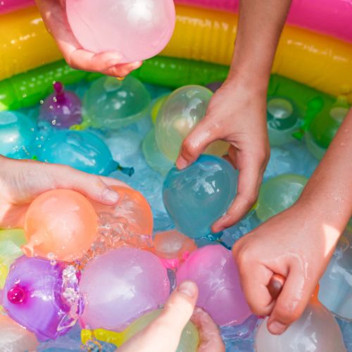 Hands reaching in to small swimming pool to grab colorful water balloons.