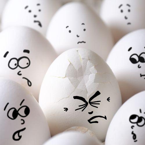 Cracked egg among all eggs with faces drawn on them.