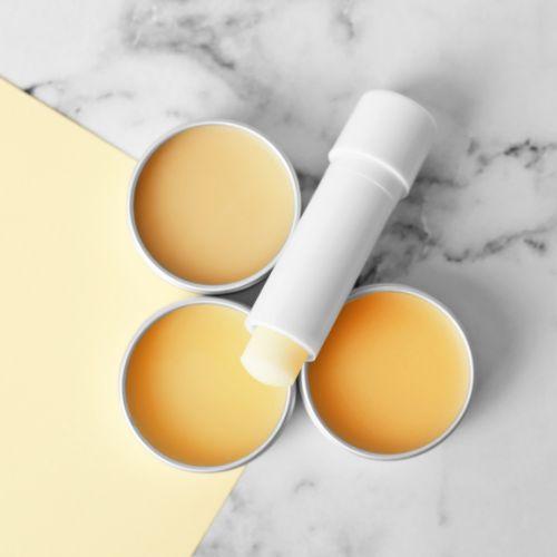Pale lip balm in three small tins and one lipstick tube on a grey and white counter.