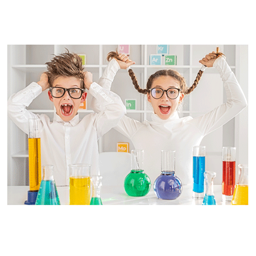 Two children in science room with counter containing science beakers filled with different colors of liquid.