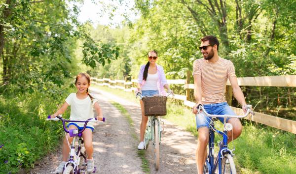 a mother, daughter and father ride bikes on a bike trail in the summer time